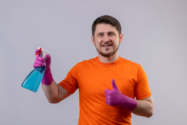 Junger Mann, der orange T-Shirt und Gummihandschuhe trägt, die Reinigungsspray halten