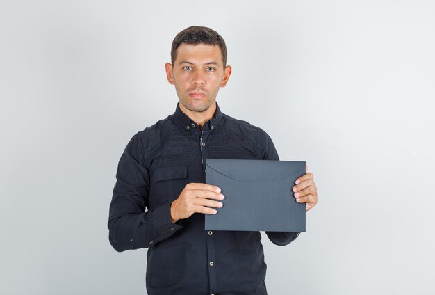 Junger Mann, der Papierumschlag im schwarzen Hemd hält