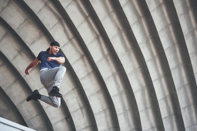 Junger Mann, der Parkour-Sprung im städtischen Raum im sonnigen Frühlingssommertag der Stadt tut.