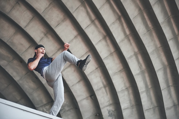 Junger Mann, der Parkour-Sprung im städtischen Raum im sonnigen Frühlingssommertag der Stadt tut.