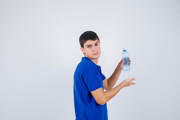 Junger Mann, der Plastikflasche im T-Shirt zeigt und zuversichtlich schaut