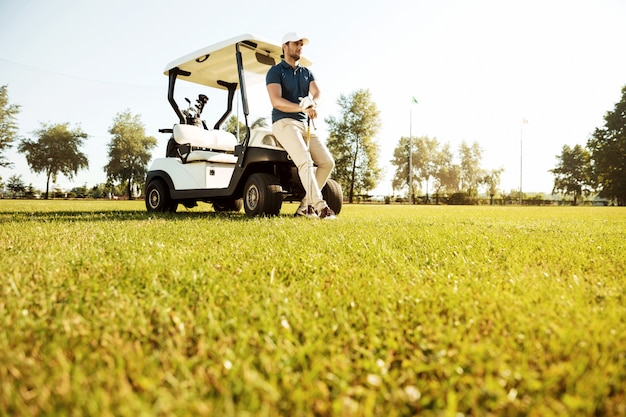 Kostenloses Foto junger mann, der ruht, während er sich auf einen golfwagen stützt