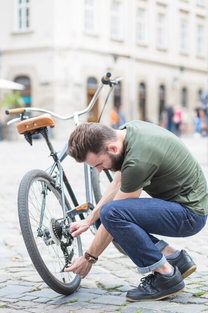 Junger Mann, der sein Fahrrad auf Straße in der Stadt repariert