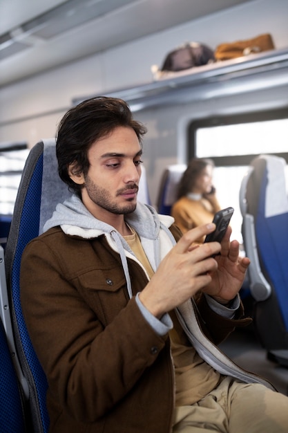 Junger Mann, der sein Smartphone benutzt, während er mit dem Zug fährt