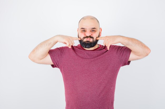 Junger Mann, der seine aufgeblasenen Finger in der Vorderansicht des rosa T-Shirts zusammendrückt.