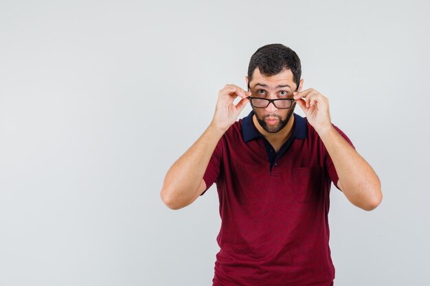 Junger Mann, der seine Brille im roten T-Shirt trägt und fokussierte Vorderansicht schaut.