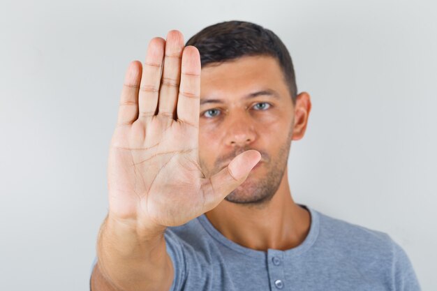 Junger Mann, der seine saubere Handfläche oben in der grauen T-Shirt-Vorderansicht zeigt.