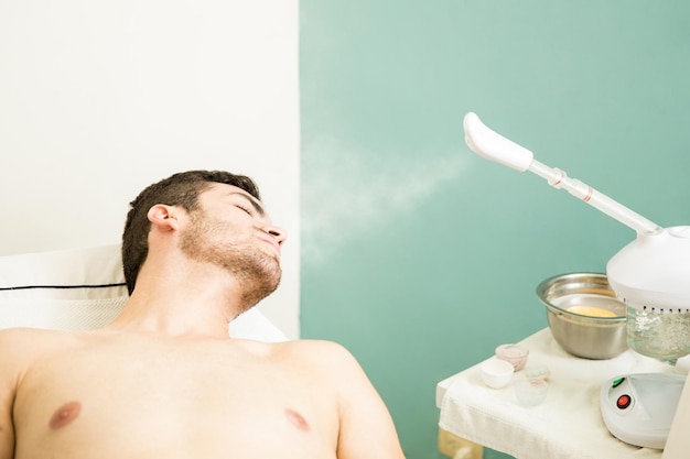 Kostenloses Foto junger mann, der sich entspannt und sich während eines besuchs in einem gesundheits-spa etwas gesichtsdampfen lässt