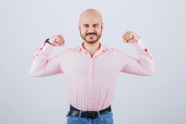 Junger Mann, der Siegergeste im Hemd, in den Jeans zeigt und glücklich schaut. Vorderansicht.