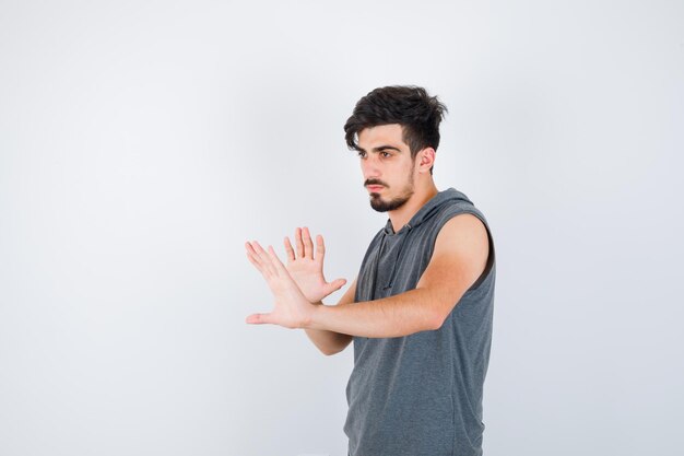 Junger Mann, der Stoppschilder in grauem T-Shirt zeigt und ernst aussieht