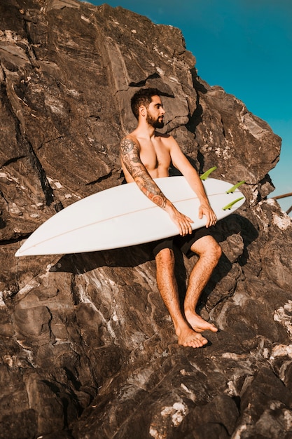 Junger Mann, der Surfbrett nahe Steinen hält