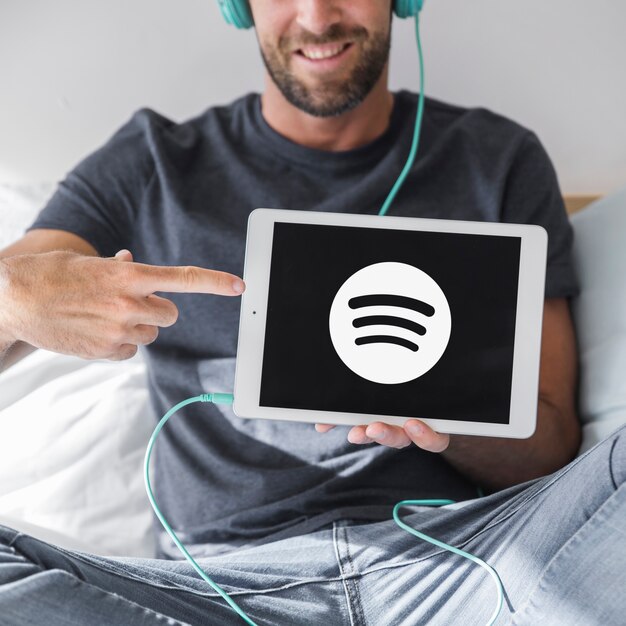 Junger Mann, der Tablette mit spotify APP hält