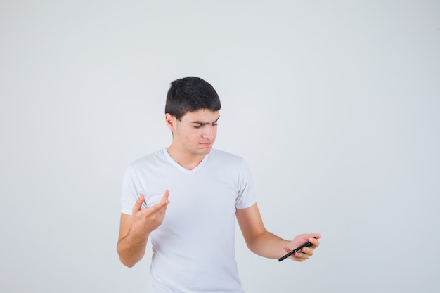 Junger Mann, der Telefon hält, während er im T-Shirt beiseite zeigt und konzentriert schaut. Vorderansicht.