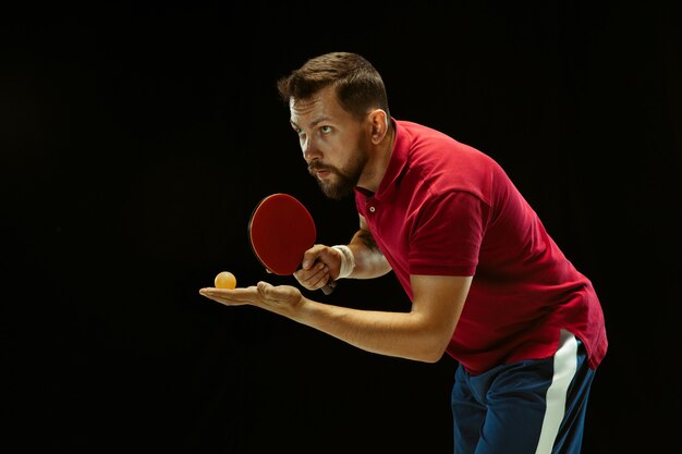 Junger Mann, der Tischtennis auf schwarzem Studio spielt