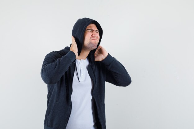 Junger Mann, der unter Nackenschmerzen im T-Shirt, in der Jacke leidet und müde aussieht. Vorderansicht.