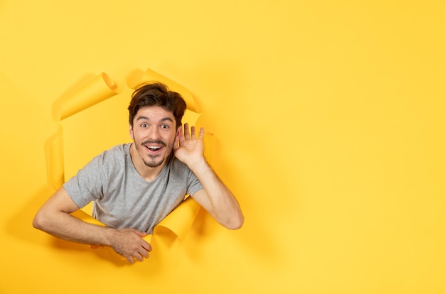 Junger Mann, der vom zerrissenen gelben Papierhintergrund Innenkerlgesichtsverkauf hört und schaut