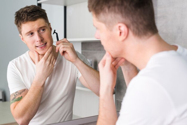 Junger Mann, der vor Spiegel im Badezimmer sich rasiert