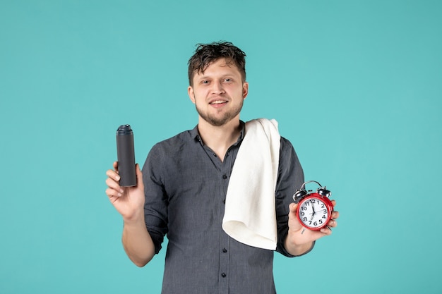 junger Mann der Vorderansicht, der eine Uhr auf blauem Hintergrund hält