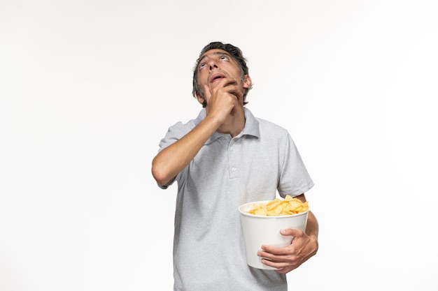 Junger Mann der Vorderansicht, der Kartoffelchips isst, während Film auf weißem Schreibtisch betrachtet