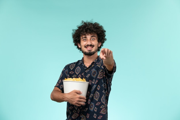 Junger Mann der Vorderansicht, der Kartoffelspitzen auf dem Filmkino des blauen Kinos des männlichen Kinos hält