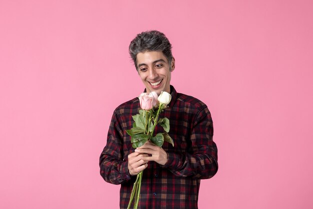 Junger Mann der Vorderansicht, der mit schönen rosa Rosen auf rosa Wand aufwirft