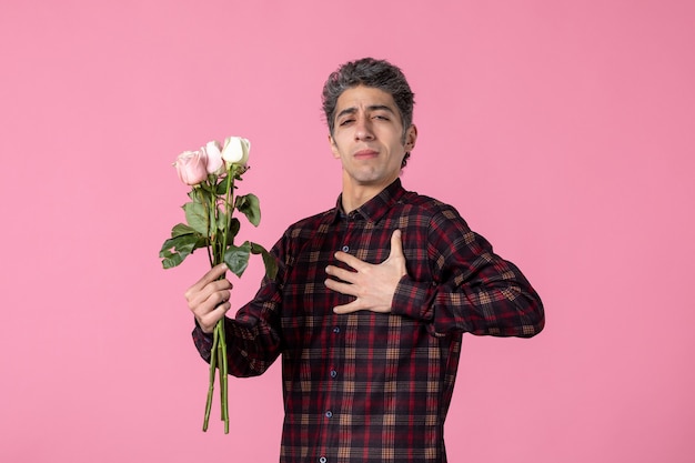 Junger Mann der Vorderansicht, der mit schönen rosa Rosen auf rosa Wand aufwirft