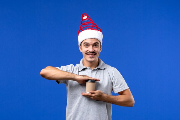 Junger Mann der Vorderansicht, der Plastikkaffeetasse auf dem männlichen Feiertag der blauen Wand des neuen Jahres hält