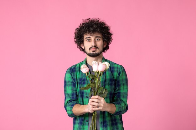 Junger Mann der Vorderansicht, der rosa Rosen auf rosa Farbe hält