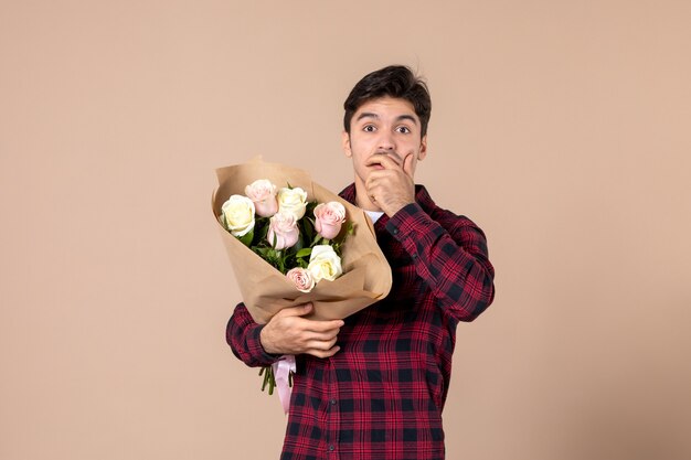 Junger Mann der Vorderansicht, der schöne Blumen auf brauner Wand hält