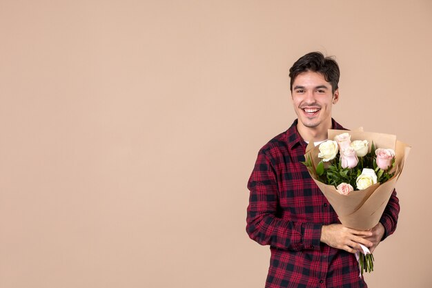 Junger Mann der Vorderansicht, der schöne Blumen auf brauner Wand hält