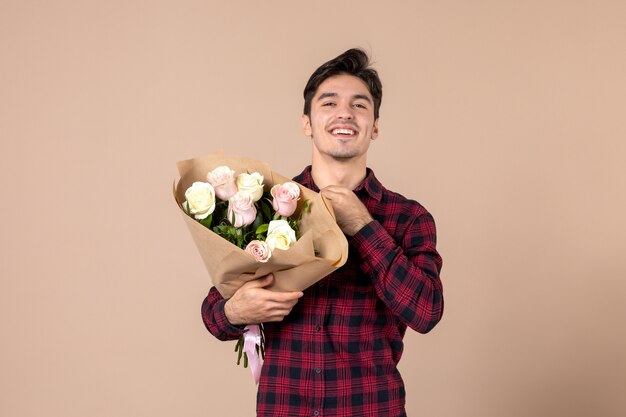 Junger Mann der Vorderansicht, der schöne Blumen auf brauner Wand hält