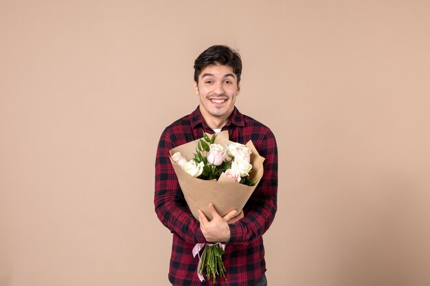 Junger Mann der Vorderansicht, der schöne Blumen auf brauner Wand hält
