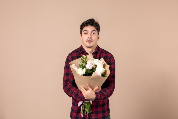 Junger Mann der Vorderansicht, der schöne Blumen auf brauner Wand hält