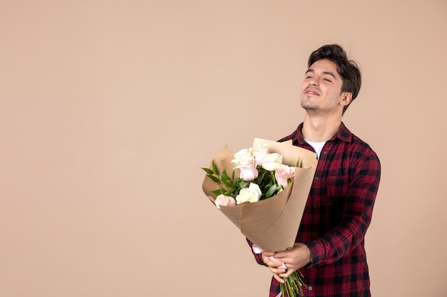 Junger Mann der Vorderansicht, der schöne Blumen auf brauner Wand hält