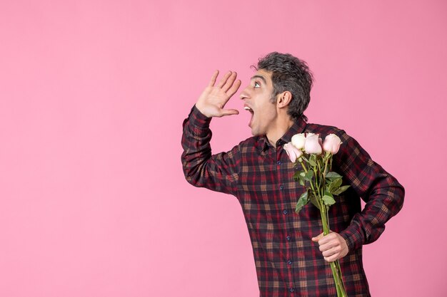 Junger Mann der Vorderansicht, der schöne rosa Rosen auf rosa Wand gibt