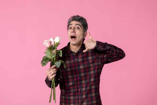 Junger Mann der Vorderansicht, der schöne rosa Rosen auf rosa Wand hält