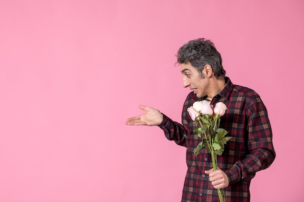 Junger Mann der Vorderansicht, der schöne rosa Rosen auf rosa Wand hält