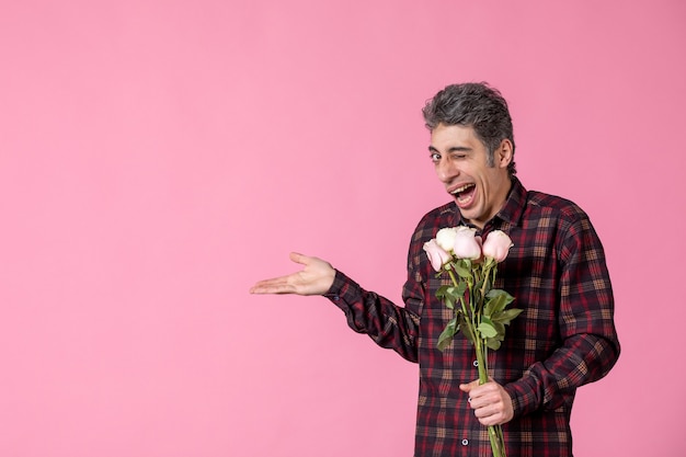 Junger Mann der Vorderansicht, der schöne rosa Rosen auf rosa Wand hält