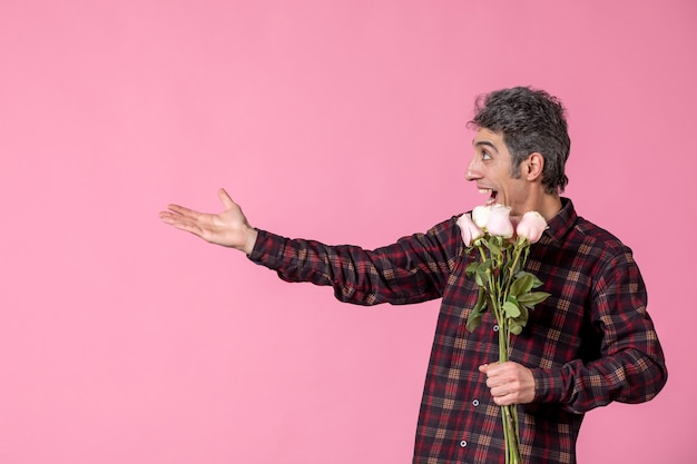 Junger Mann der Vorderansicht, der schöne rosa Rosen auf rosa Wand hält