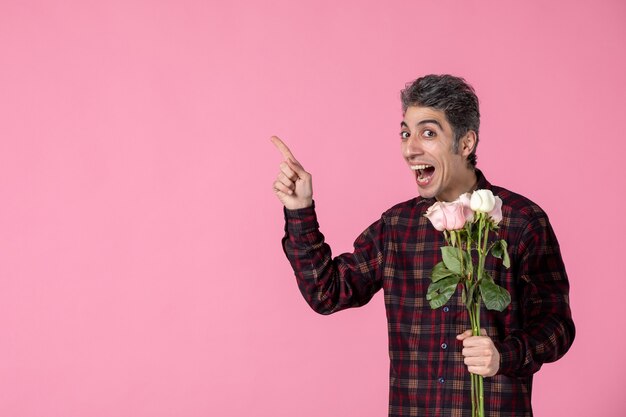 Junger Mann der Vorderansicht, der schöne rosa Rosen auf rosa Wand hält