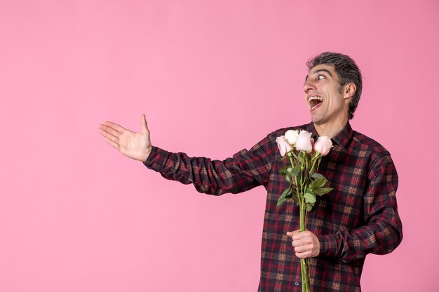 Junger Mann der Vorderansicht, der schöne rosa Rosen auf rosa Wand hält