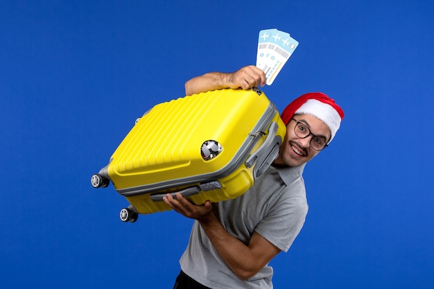 Junger Mann der Vorderansicht, der schwere Tasche mit Tickets auf Urlaubsflugzeug der blauen Wandflüge trägt