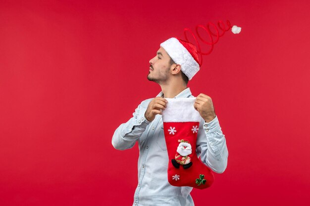 Junger Mann der Vorderansicht, der Weihnachtssocke auf rotem Schreibtischfeiertagsweihnachten hält