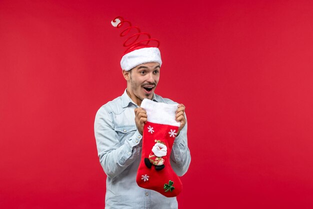 Junger Mann der Vorderansicht, der Weihnachtssocke auf rotem Schreibtischweihnachtsfeiertag hält
