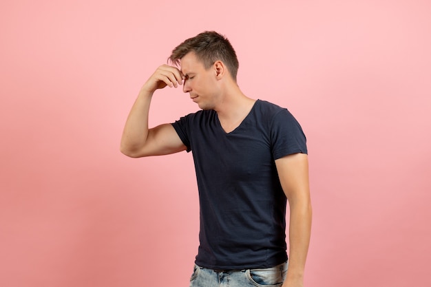 Junger Mann der Vorderansicht im blauen T-Shirt, das unter Kopfschmerzen auf einem männlichen Emotionsfarbmodellmensch des rosa Hintergrundes leidet