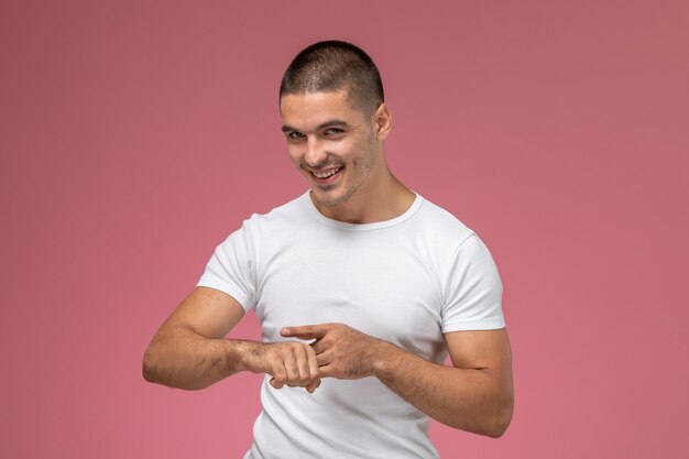 Junger Mann der Vorderansicht im weißen Hemd, das auf sein Handgelenk mit Lächeln auf rosa Hintergrund hinweist