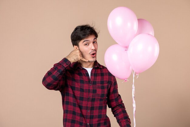 Junger Mann der Vorderansicht mit rosa Luftballons auf brauner Wand
