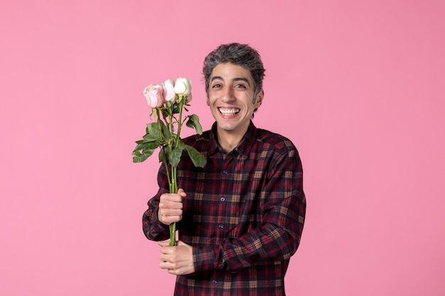 Junger mann der vorderansicht mit schönen rosa rosen, die auf rosa wand lächeln