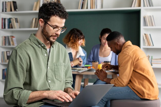 Junger Mann, der während der Studiengruppe seinen Laptop für Informationen verwendet