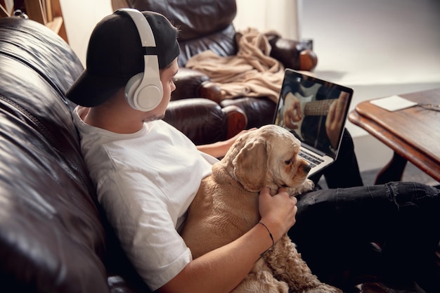 Junger Mann, der während des Coronavirus mit seinem Hundehaustier spielt und Musik hört